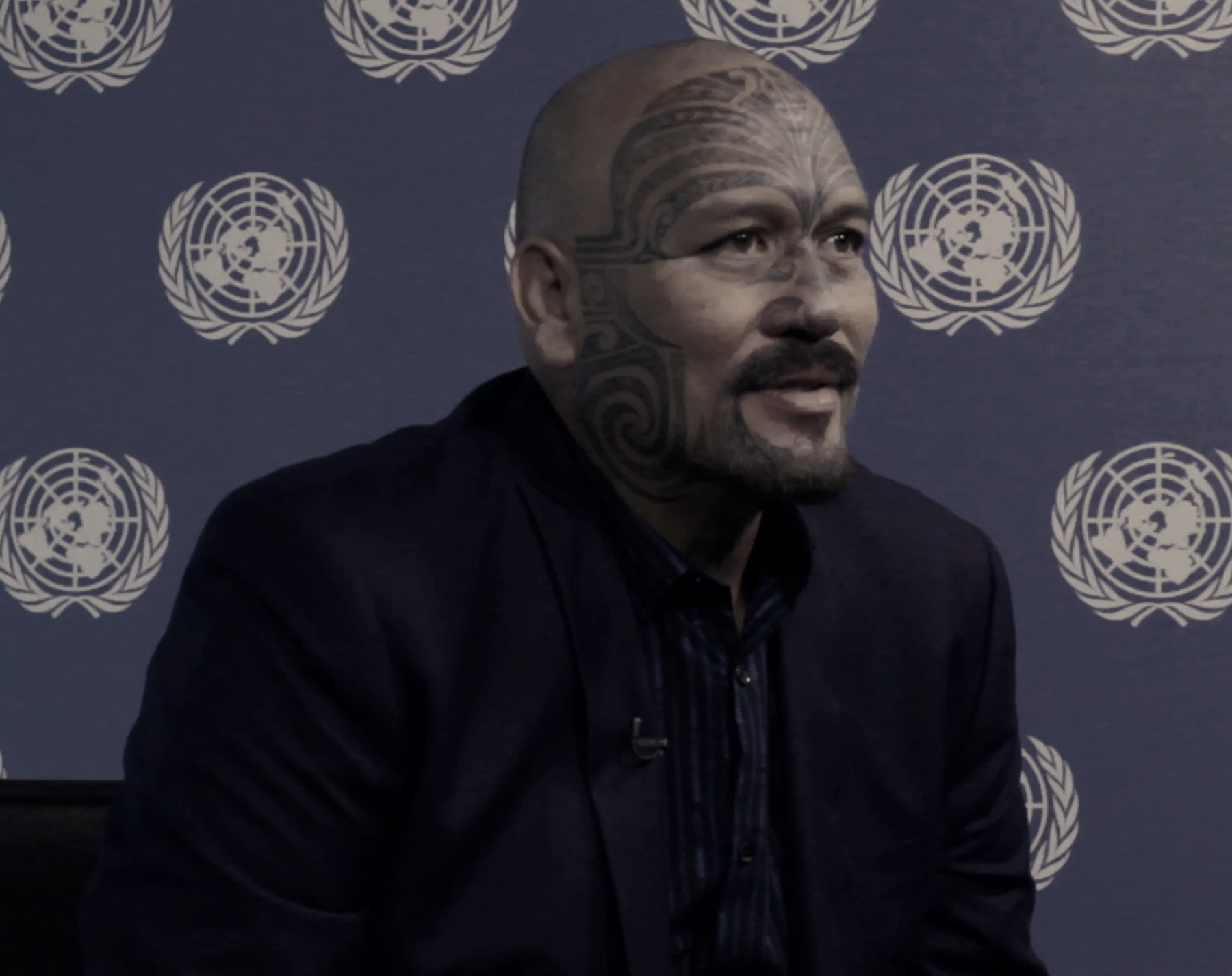 The Ali'i Nui with full facial moko seated before a United Nations backdrop